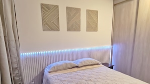 Un dormitorio con cama, cortinas, un radiador y cuadros en la pared.
