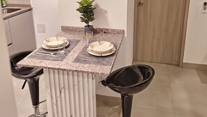 Una cocina moderna con encimera de mármol, dos taburetes de bar, una planta en maceta y una puerta.