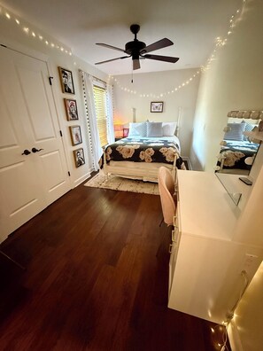 Une chambre à coucher avec un lit, un bureau, une chaise, un ventilateur de plafond et des guirlandes lumineuses.