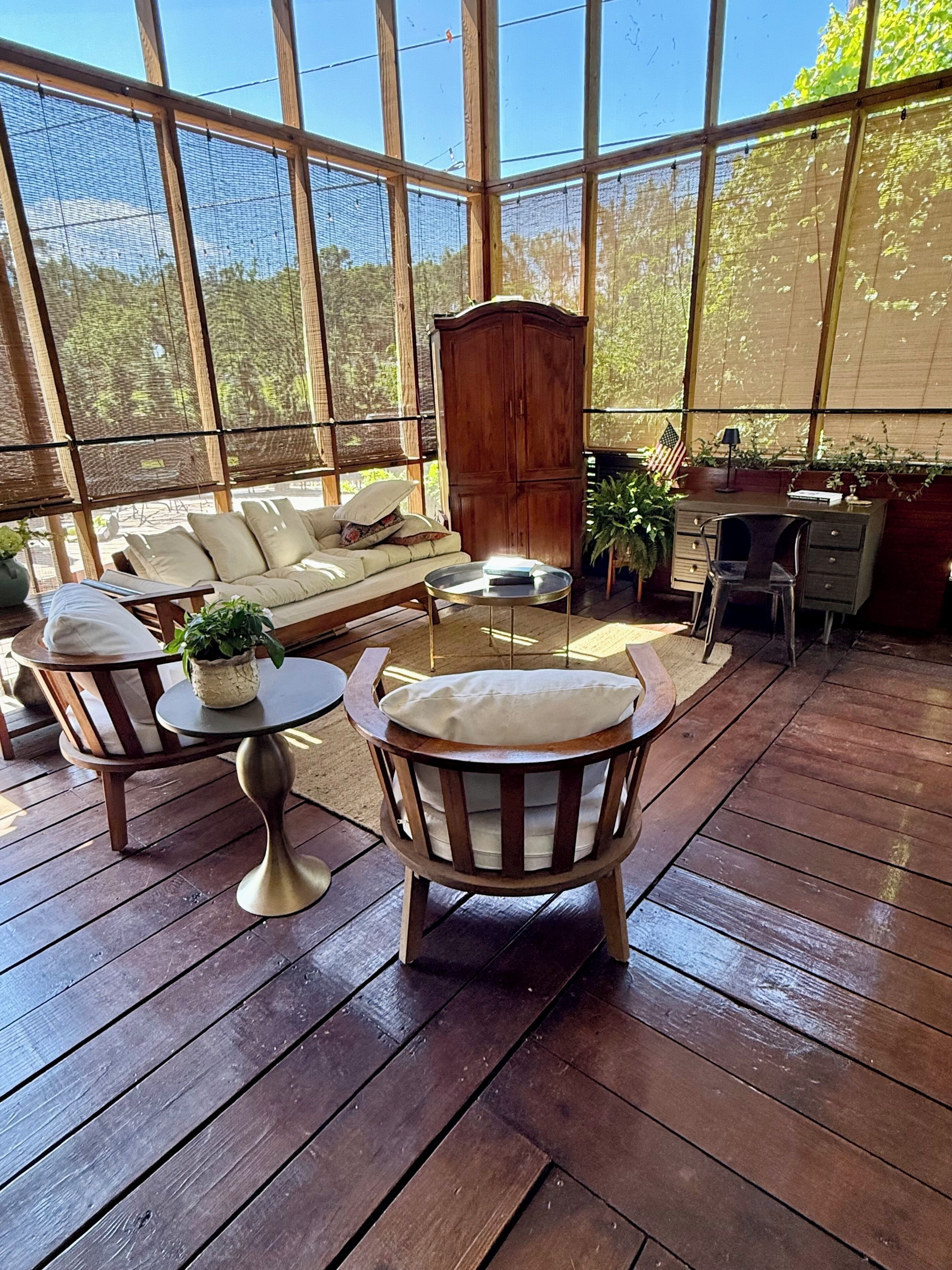 A sunlit wooden deck with a sofa, chairs, and a small table.