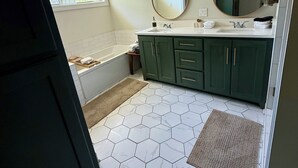 A bathroom with a bathtub, a sink, green cabinets, a large mirror, and hexagonal patterned flooring. - Oxford at its Best! Location, Layout, Privacy!! (Oxford)