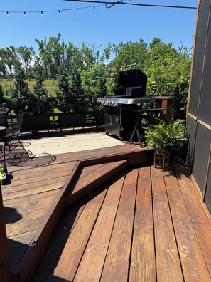 Une terrasse en bois équipée d’un barbecue, de mobilier d’extérieur et offrant une vue sur un cimetière en arrière-plan.