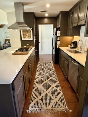 A modern kitchen with dark cabinetry, a central island, and a patterned rug. - Oxford at its Best! Location, Layout, Privacy!! (Oxford)