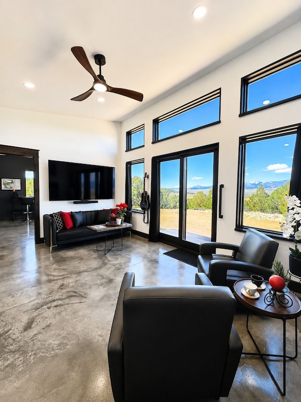 A modern living room with a black leather sofa, a coffee table, and a ceiling fan.