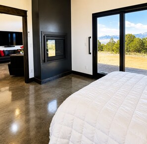 A bedroom with a large bed, a fireplace, and a view of a mountainous landscape. - Modern Mountain Escape 2 Bed, 2 Bath 360 degree Sangre Views (Westcliffe)