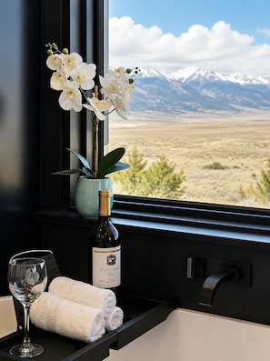 A window with a view of a mountainous landscape, a bottle of Hobson Estate wine, a glass of wine, and a rolled towel on a shelf. - Modern Mountain Escape 2 Bed, 2 Bath 360 degree Sangre Views (Westcliffe)