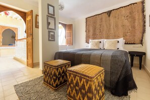 A bedroom with a large bed, two woven stools, a textured headboard, and a view of a courtyard. - 4-bedroom riad in charming Marrakesh with cool AC (Marrakesh)