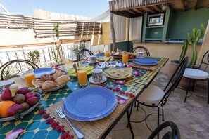 An outdoor dining area with a table set for breakfast, including fruits, pastries, and beverages. - 4-bedroom riad in charming Marrakesh with cool AC (Marrakesh)