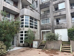 Ein mehrstöckiges Gebäude mit Hauseingang an der Ecke, Außentreppe und einem kleinen Garten mit Pflanzen.