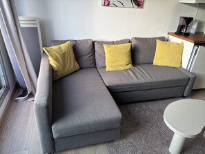 Ein graues Ecksofa mit gelben Kissen, ein weißer Couchtisch und eine Heizung.