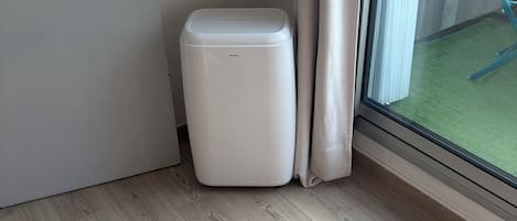 A room with a wooden floor, a white trash bin, a door, and a window with a view of a green outdoor area.