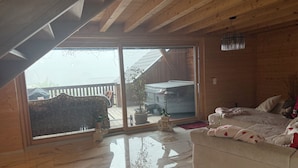 A room with a wooden ceiling, a sliding glass door leading outside, a sofa, and a bed with pillows and blankets.