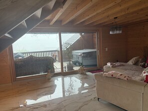 A room with a wooden ceiling, a sliding glass door leading outside, a sofa, and a bed with pillows and blankets.