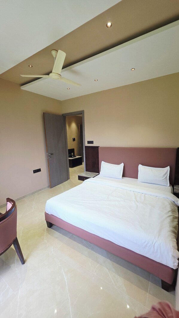 Una habitación de hotel moderna con una cama grande, un ventilador de techo y un pequeño rincón de descanso.