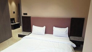 A modern hotel room with a large bed, a nightstand, and a wall-mounted TV. - The VSK Stays (Igatpuri)