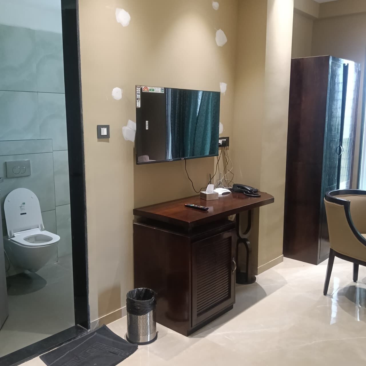 A bathroom with a toilet, a sink with a mirror, a trash bin, and a chair.