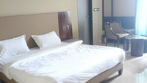 A hotel room with a large bed, a wooden headboard, a chair, a small table, and a mirror. - The VSK Stays (Igatpuri)
