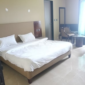 A hotel room with a large bed, a wooden headboard, a chair, a small table, and a mirror.