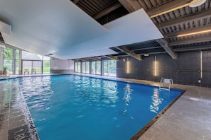 An indoor swimming pool with clear glass walls, a tiled floor, and a ceiling with exposed beams. - Stunning 2-bedroom condo with pools and spa! (Beaupré)