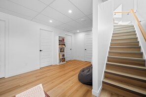 A clean, modern room with wooden flooring, white walls, a built-in bookshelf, and a staircase with wooden steps.