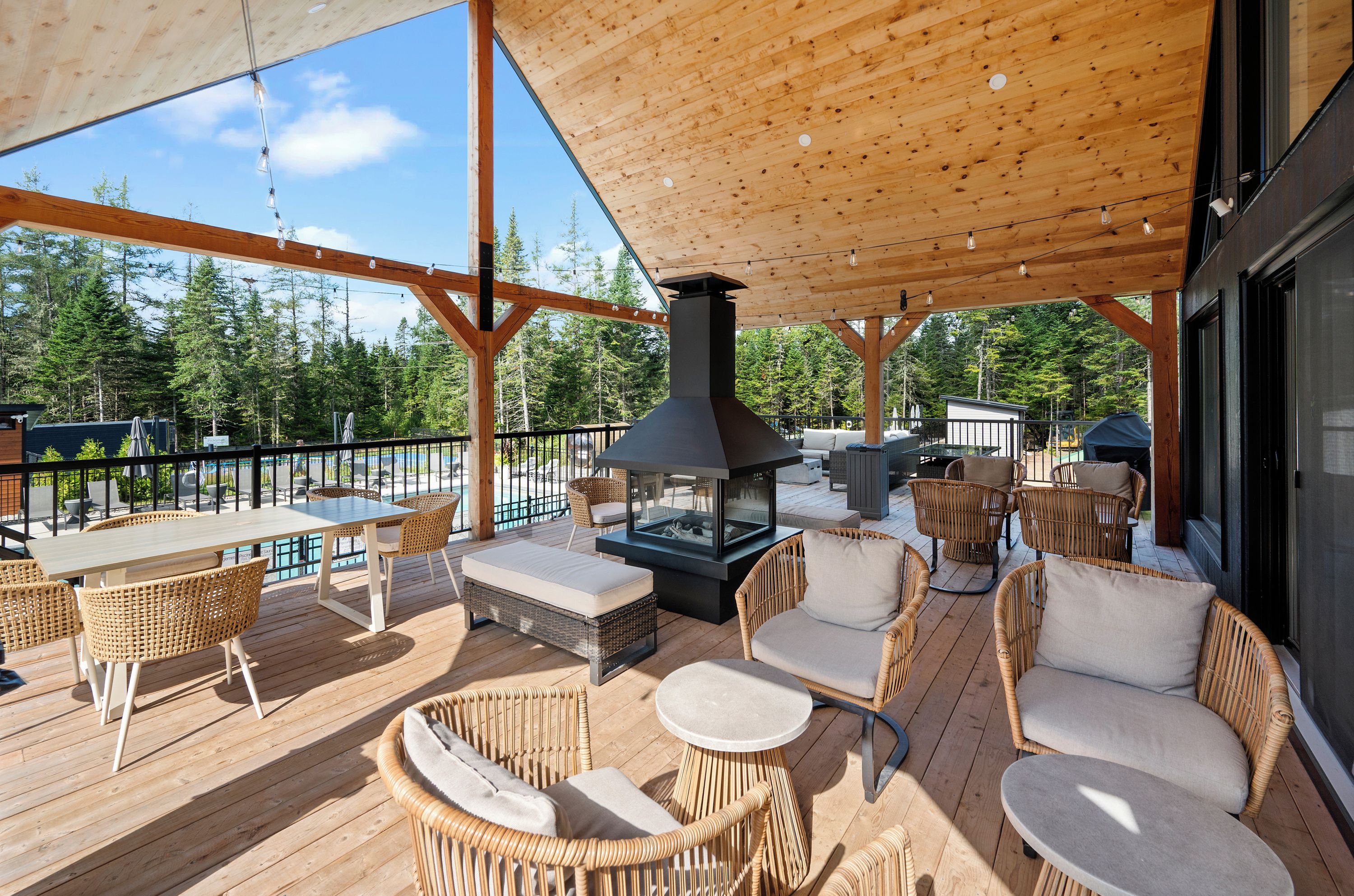 Une terrasse extérieure avec un plancher en bois, des meubles en osier, une cheminée intégrée et une vue sur une forêt.