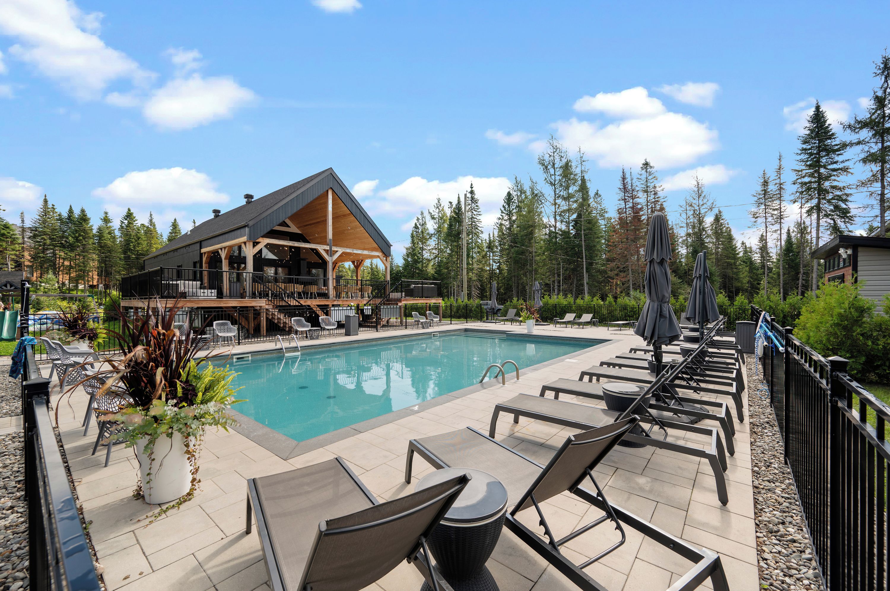 Un espace aménagé au bord de la piscine, avec des chaises longues, une terrasse en bois et un bâtiment doté d’un toit en pente.