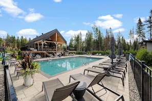 A poolside area with lounge chairs, a wooden deck, and a building with a sloped roof.