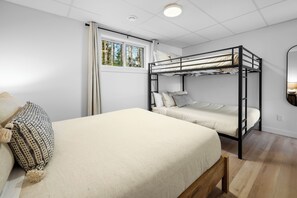 A bunk bed room with a window, a bedside table with a lamp, and a bed with a pillow.