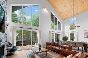 A spacious living room with a large window, a wooden ceiling, and a dining area with a view of the outdoors.