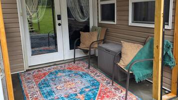 A covered porch with a patterned rug, a bench, and a door with curtains.