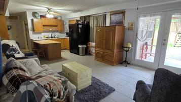 A spacious living area with a sofa, a wooden coffee table, and a dining table. A kitchen with cabinets and a refrigerator is visible in the background.