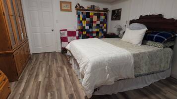 A bedroom with a bed, wooden flooring, a ceiling fan, a wardrobe, and a quilted curtain.