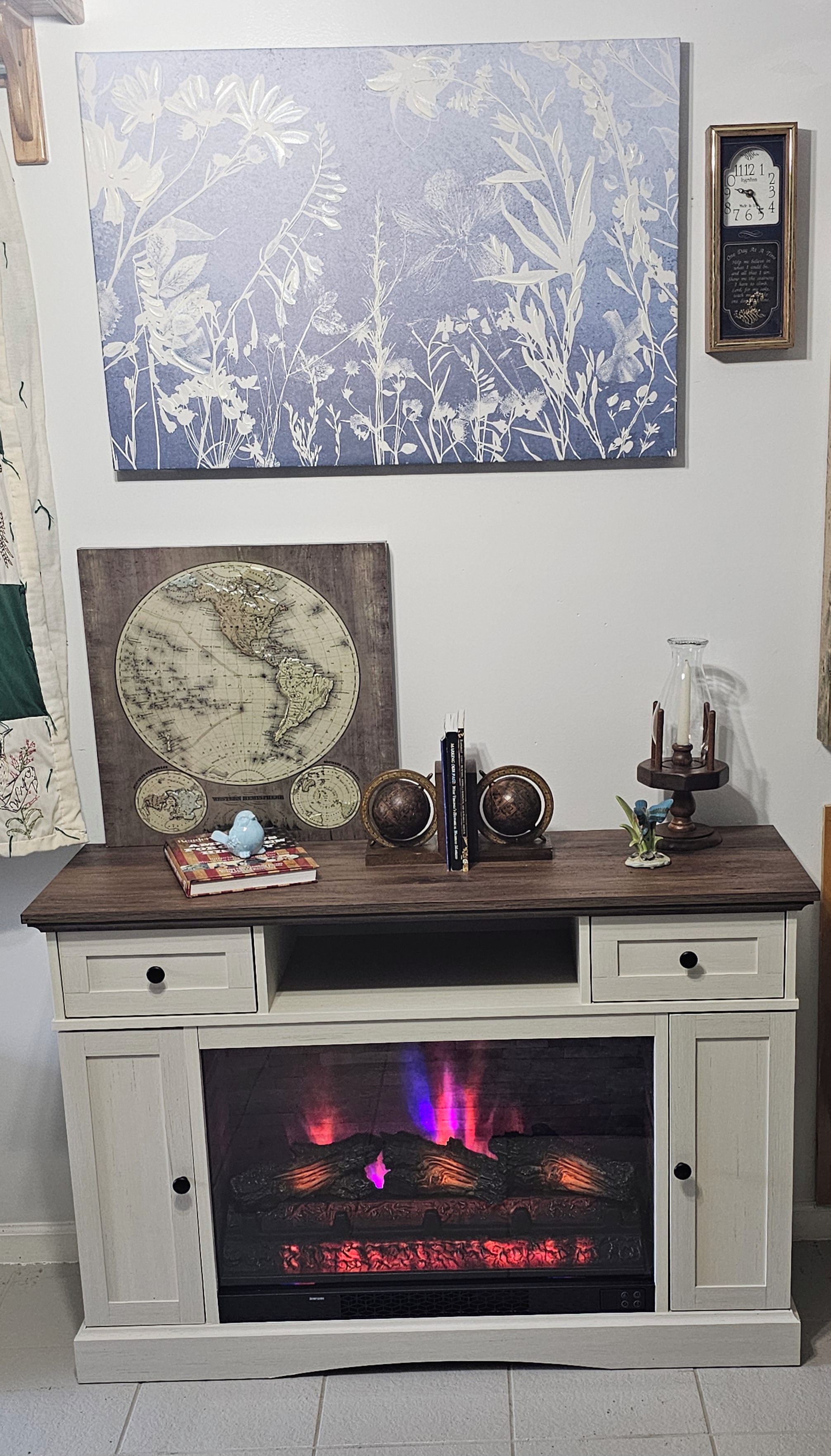 A fireplace with a modern design, a world map, decorative globes, and a framed floral artwork above it.