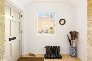 Ein Zimmer mit einer weißen Tür, einem Fenster mit Blick auf ein Gebäude, einem Kleiderständer mit Stiefeln und einer Vase mit Regenschirmen.