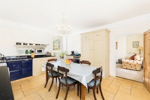 A well-lit kitchen with a dining table, chairs, and a chandelier. - The Village Farmhouse | Cotswolds | Sleeps 6 - Pass the Keys (Cirencester)