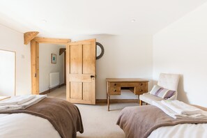Ein Schlafzimmer mit zwei Betten, einem Holztisch, einem Heizkörper und einer Tür zu einem anderen Raum.