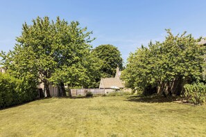 A grassy backyard with a stone building, surrounded by trees. - The Village Farmhouse | Cotswolds | Sleeps 6 - Pass the Keys (Cirencester)