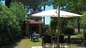 Un'area patio esterna con un tavolo e sedie, circondata da vegetazione e un edificio con tetto in tegole.
