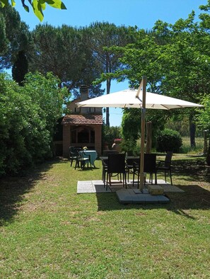 An outdoor patio area with a table and chairs, surrounded by greenery and a building with a tiled roof. - Apartment in an old farmhouse in the Tuscan countryside, 3.5 km from the sea. (Toscana)