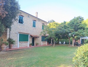 A stone building with green shutters, a lawn, and trees. - Apartment in an old farmhouse in the Tuscan countryside, 3.5 km from the sea. (Toscana)