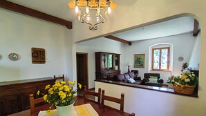 Zona pranzo con tavolo in legno, sedie, un lampadario e vista sul soggiorno.