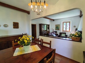 A dining area with a wooden table, chairs, a chandelier, and a view into the living room. - Apartment in an old farmhouse in the Tuscan countryside, 3.5 km from the sea. (Toscana)