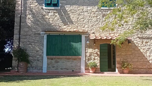 Un edificio in pietra con un'ampia finestra e un portone, circondato da un prato curato.
