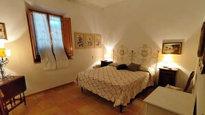 Una camera da letto con un letto, due comodini, un tavolo da notte, una finestra con tende e una parete decorata con quadri.
