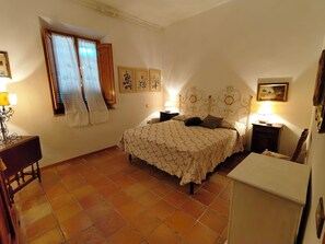 A bedroom with a bed, two bedside tables, a nightstand, a window with curtains, and a wall with framed pictures. - Apartment in an old farmhouse in the Tuscan countryside, 3.5 km from the sea. (Toscana)