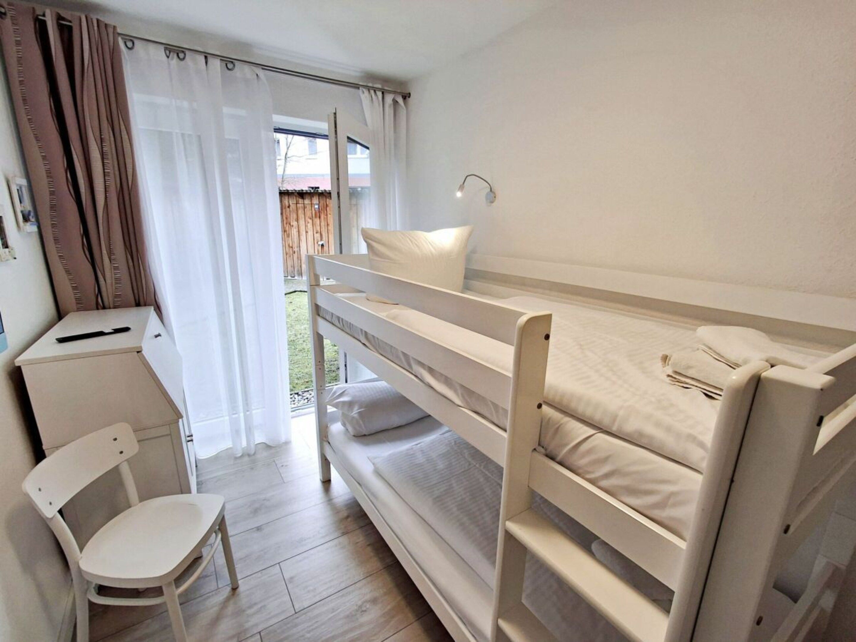 A bunk bed room with a desk and chair, a window with curtains, and a view of the outside.