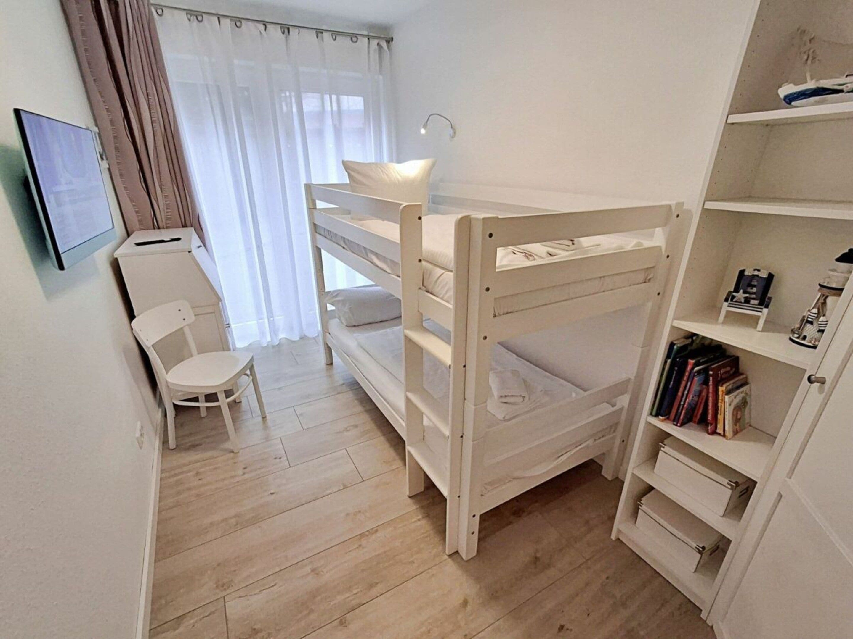 A room with a bunk bed, a desk, a chair, and a bookshelf.