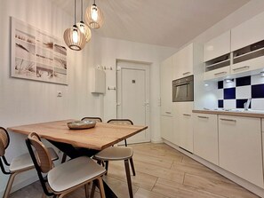 A modern kitchen with white cabinets, a wooden dining table, and a hanging light fixture. - Villa Bettina Apartment 03 (Heringsdorf)