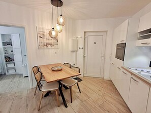 A modern kitchen with white cabinets, a wooden dining table, and a hanging light fixture. - Villa Bettina Apartment 03 (Heringsdorf)