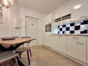 Cozinha moderna com armários brancos, painel de fundo xadrez e área de refeições com mesa e cadeiras de madeira.